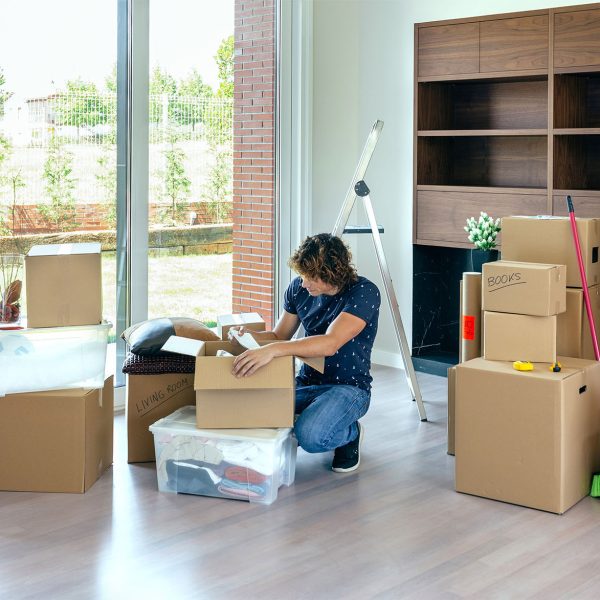Young man unpacking moving boxes in living room